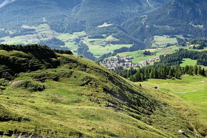 Blick zurück zum Dorf Ftan. Die grüne Hügel sind von Morgensonne